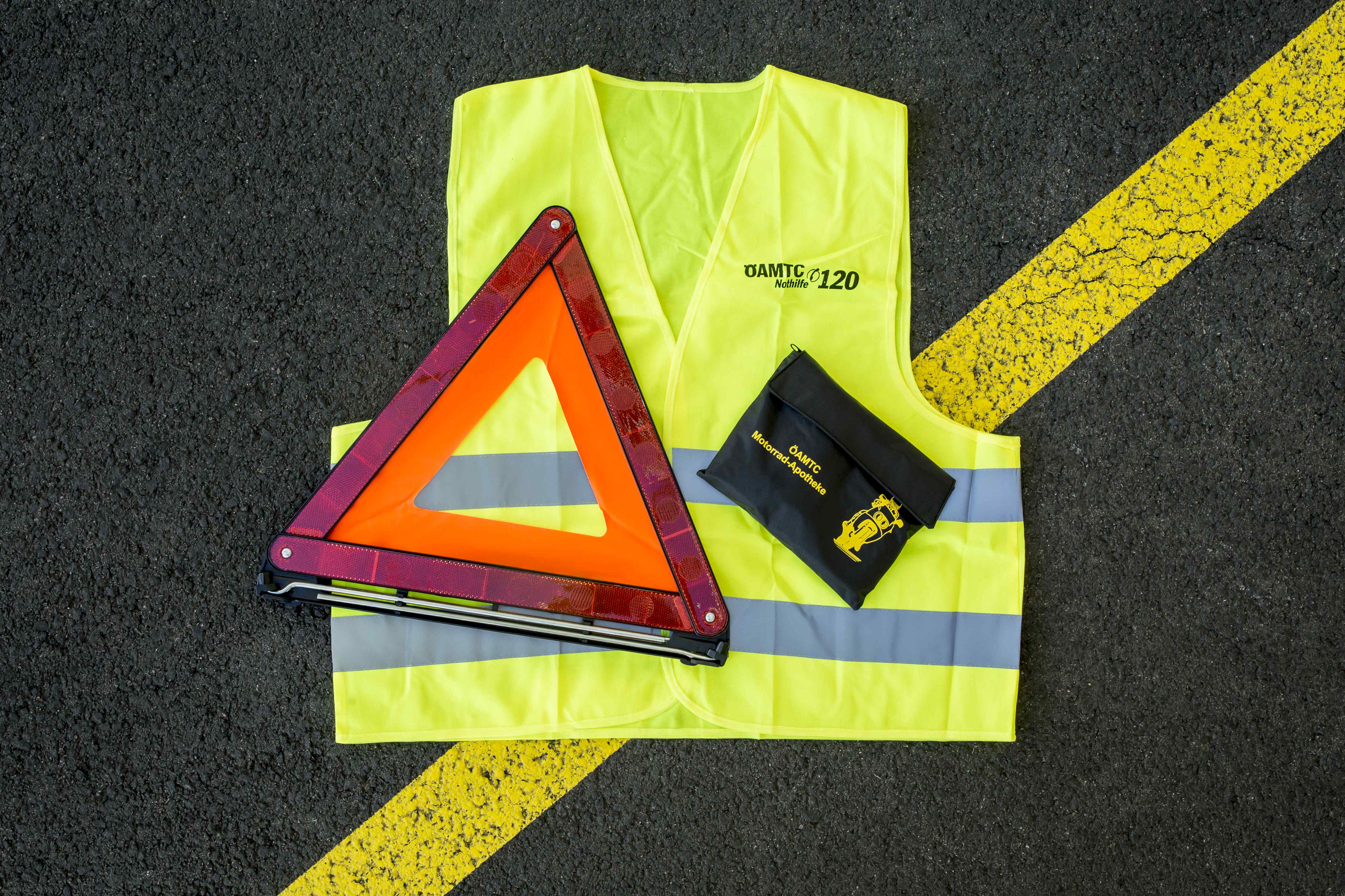 Auf einer Straße liegt eine Warnweste, ein Pannendreieck, eine Motorradapotheke.