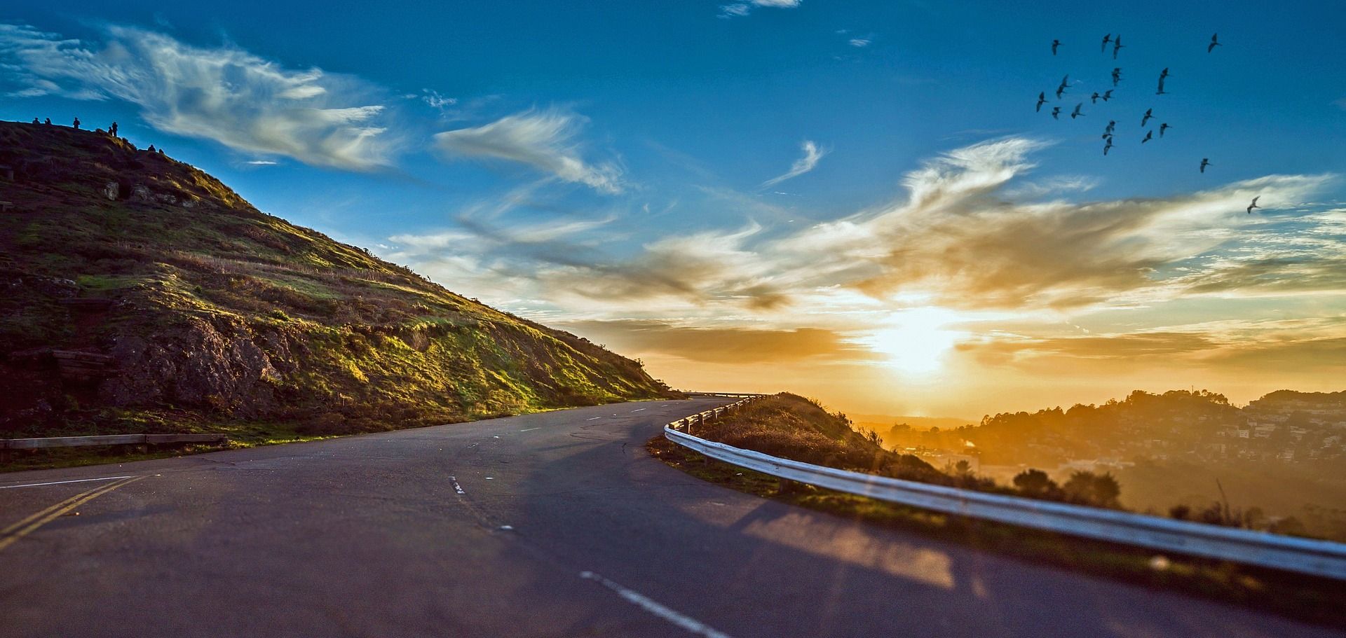 Eine Straße schlängelt sich um einen Hügel, mit einem Sonnenuntergang im Hintergrund.