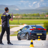Ein Instruktor der ÖAMTC Fahrtechnik gibt einem Trainings-Teilnehmenden Anweisungen über sein Funkgerät, während der Teilnehmende mit seinem Auto einen Slalom-Parcour absolviert.