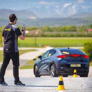 Ein Instruktor der ÖAMTC Fahrtechnik gibt einem Trainings-Teilnehmenden Anweisungen über sein Funkgerät, während der Teilnehmende mit seinem Auto einen Slalom-Parcour absolviert.