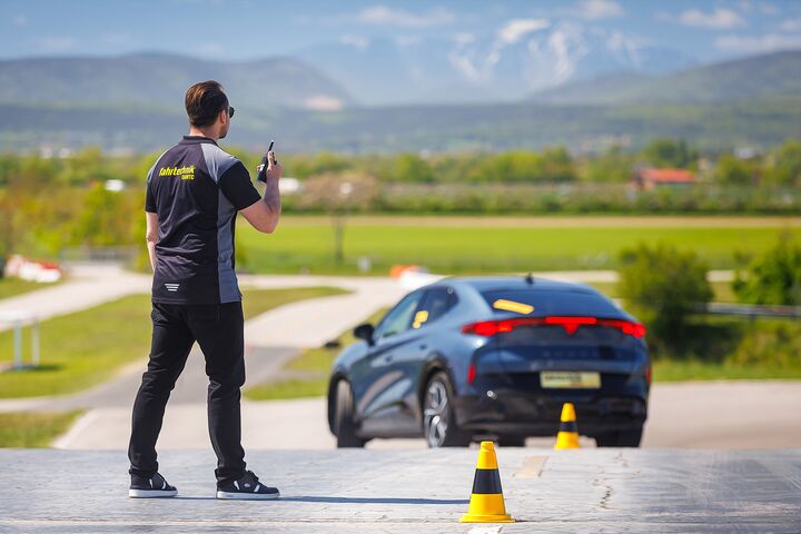 Ein Instruktor der ÖAMTC Fahrtechnik gibt einem Trainings-Teilnehmenden Anweisungen über sein Funkgerät, während der Teilnehmende mit seinem Auto einen Slalom-Parcour absolviert.