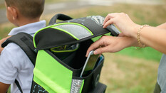 Ein Junge trägt einen Schultasche die offen ist. Man sieht eine Hand, die ein Handy in die Schultasche steckt.
