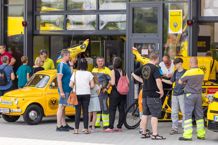Besucher:innen vor dem Stützpunk Melk im Gespräch mit Pannenfahrer, im Hintergrund befindet sich der Stützpunkt und die Pannenflotte.