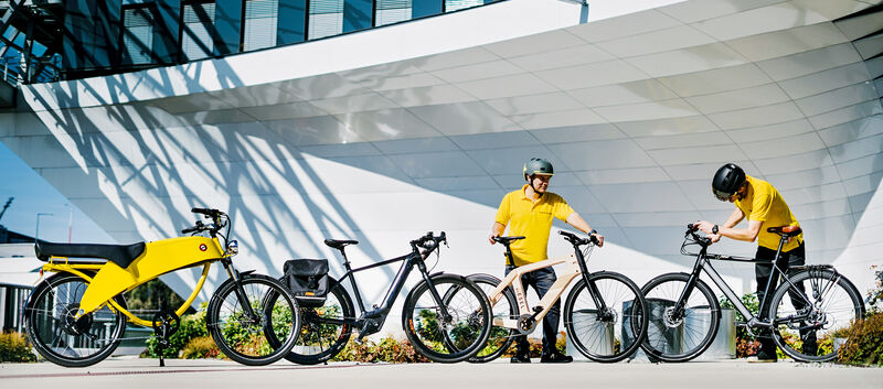 Vier Pedelecs stehen aufgereiht vor einem Gebäude. Mit im Bild sind auch zwei auto touring-Redakteure.