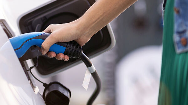 Ein weißes Elektroauto mit Ladekabel, eine Frau hält den Ladestecker in der rechten Hand.