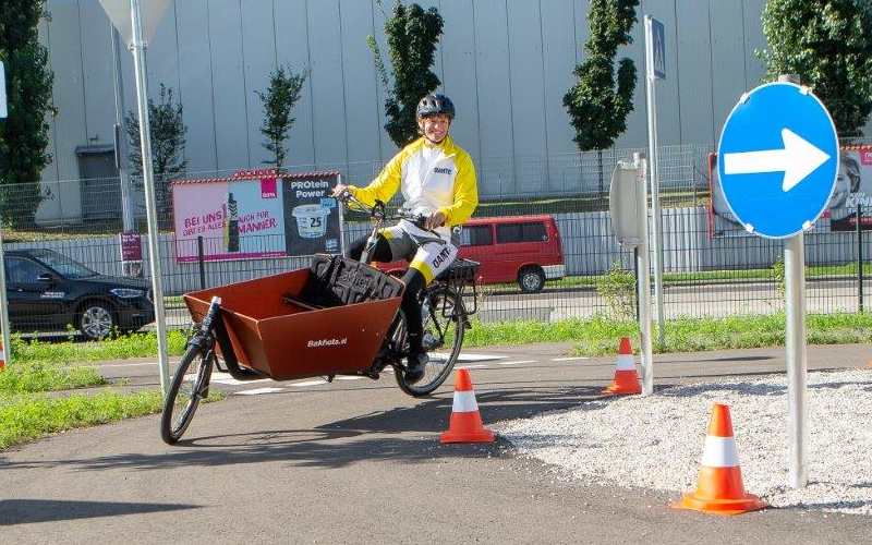 ÖAMTC-Trainerin fährt auf dem ÖAMTC Mobilitätspark mit einem Lastenfahrrad, einem Frontlader, um eine Kurve.