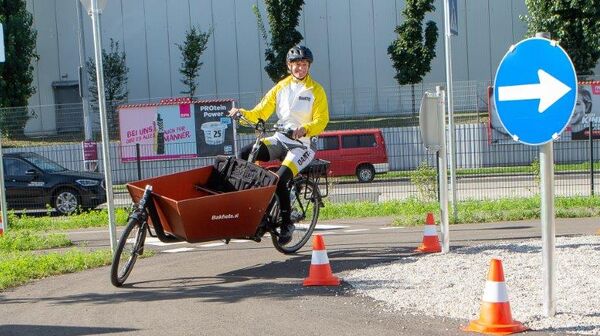 ÖAMTC-Trainerin fährt auf dem ÖAMTC Mobilitätspark mit einem Lastenfahrrad, einem Frontlader, um eine Kurve.
