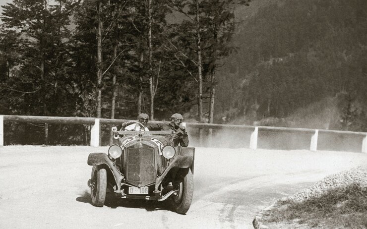 Archivbild eines Oldtimers mit zwei Personen die im Fahrzeug sitzen und am Gaisbergrennen teilnehmen. Das Fahrzeug fährt gerade um eine Kurve den Berg abwärts.