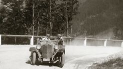 Archivbild eines Oldtimers mit zwei Personen die im Fahrzeug sitzen und am Gaisbergrennen teilnehmen. Das Fahrzeug fährt gerade um eine Kurve den Berg abwärts.