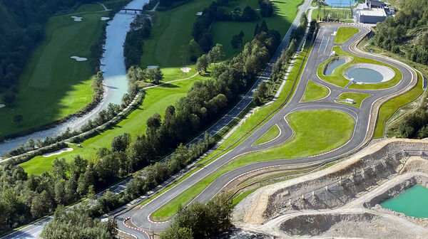 Inmitten einer ländlichen Landschaft erstreckt sich das Experience Center Saalfelden/Brandlhof. Eine große asphaltierte Übungsfläche, mit Kreuzungselementen und Übungsstraßen. Links der Übungsfläche sind eine Bundesstraße, Wiesen, ein Fluss mit zwei Brücken und ein anschließender Wald.