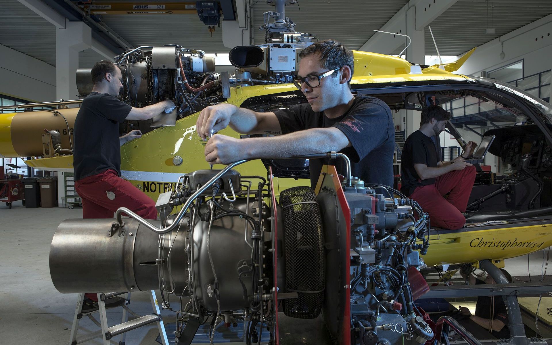 2 Techniker servicieren in einer Wartungs-Halle der HeliAir Triebwerk und Hauptrotor eines Christophorus-Hubschraubers.