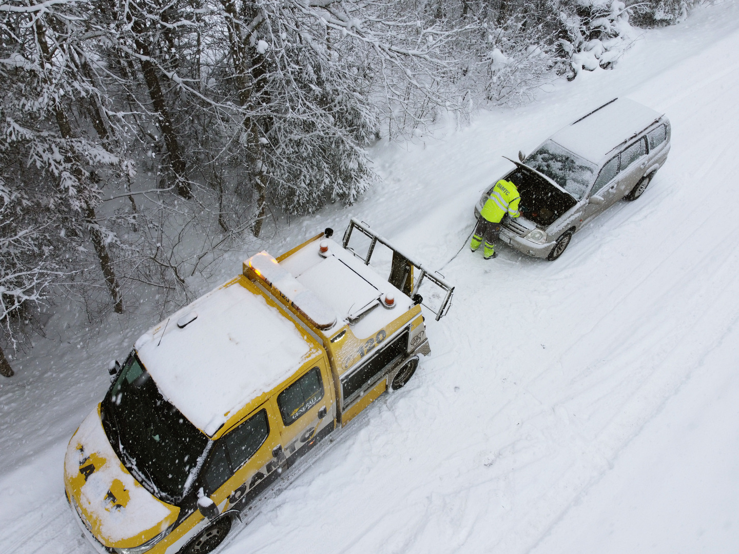 Ein ÖAMTC-Pannenfahrzeug schleppt ein anderes Fahrzeug in winterlicher Landschaft ab