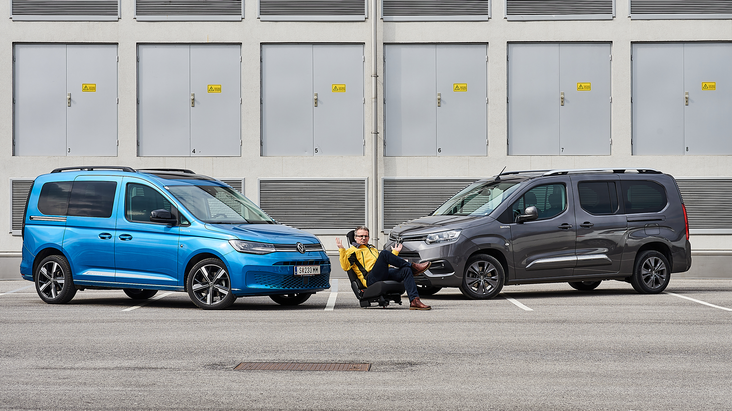Im Bild sieht man links einen hellblauen VW Caddy und rechts einen dunkelblauen Toyota Proace City Verso, zwischen den beiden sitzt ein auto touring-Redakteur.