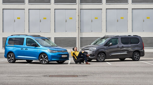Im Bild sieht man links einen hellblauen VW Caddy und rechts einen dunkelblauen Toyota Proace City Verso, zwischen den beiden sitzt ein auto touring-Redakteur.
