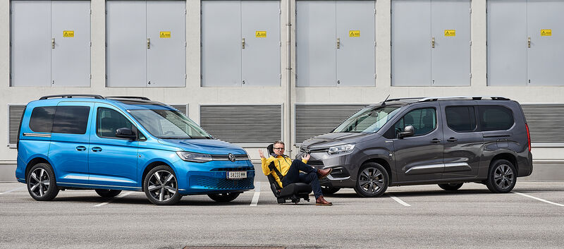 Im Bild sieht man links einen hellblauen VW Caddy und rechts einen dunkelblauen Toyota Proace City Verso, zwischen den beiden sitzt ein auto touring-Redakteur.