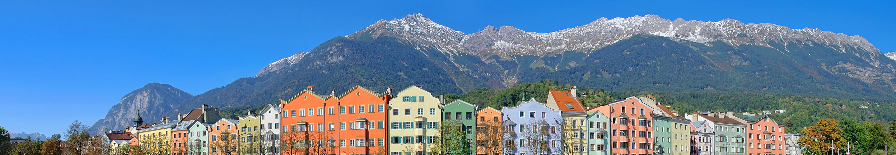 Die Häuserfassaden am Inn beeindrucken mit ihrer traditionellen Architektur und farbenfrohen Gestaltung, die eine attraktive Szenerie vor dem Bergpanorama schaffen.