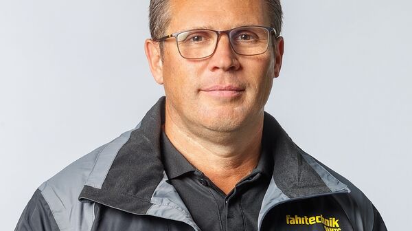 Das Bild ist ein Portrait von Roland Frisch, der frontal in die Kamera schaut und eine schwarze Jacke mit gelber ÖAMTC Fahrtechnik-Aufschrift trägt.