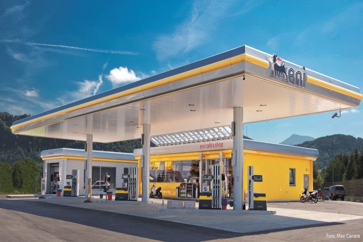 Eni Tankstelle mit Zapfsäulen, Waschanlage und Shop. Im Hintergrund blauer Himmel und Berge.