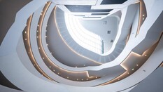 Das Atrium des Mobilitätszentrum von unten nach oben fotografiert. Das Stiegenhaus ist weiß, rund, weit und offen und das Dach ist aus Glas, sodass natürliches Licht einfällt.