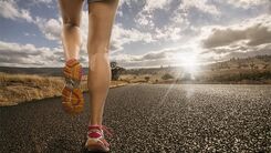 Eine Frau joggt auf einer Straße, umgeben von Sonnenlicht.