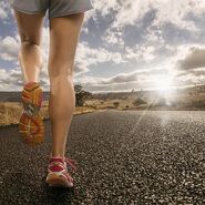 Eine Frau joggt auf einer Straße, umgeben von Sonnenlicht.