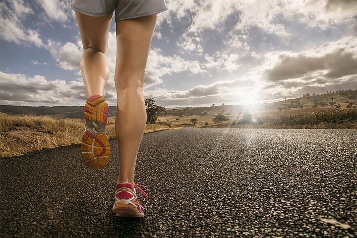 Eine Frau joggt auf einer Straße, umgeben von Sonnenlicht.
