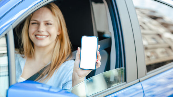 Junge Frau zeigt ihr Handy durch das Fenster des Autos.