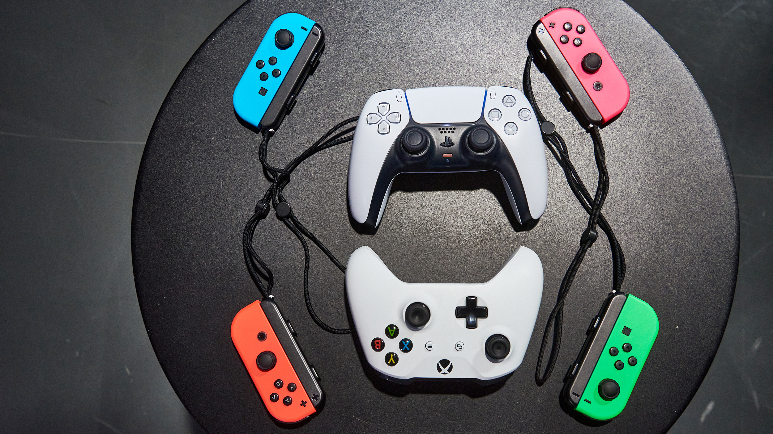 Ein Playstation, ein Xbox und 4 Switch Controller aufgelegt auf einem schwarzen Tisch.