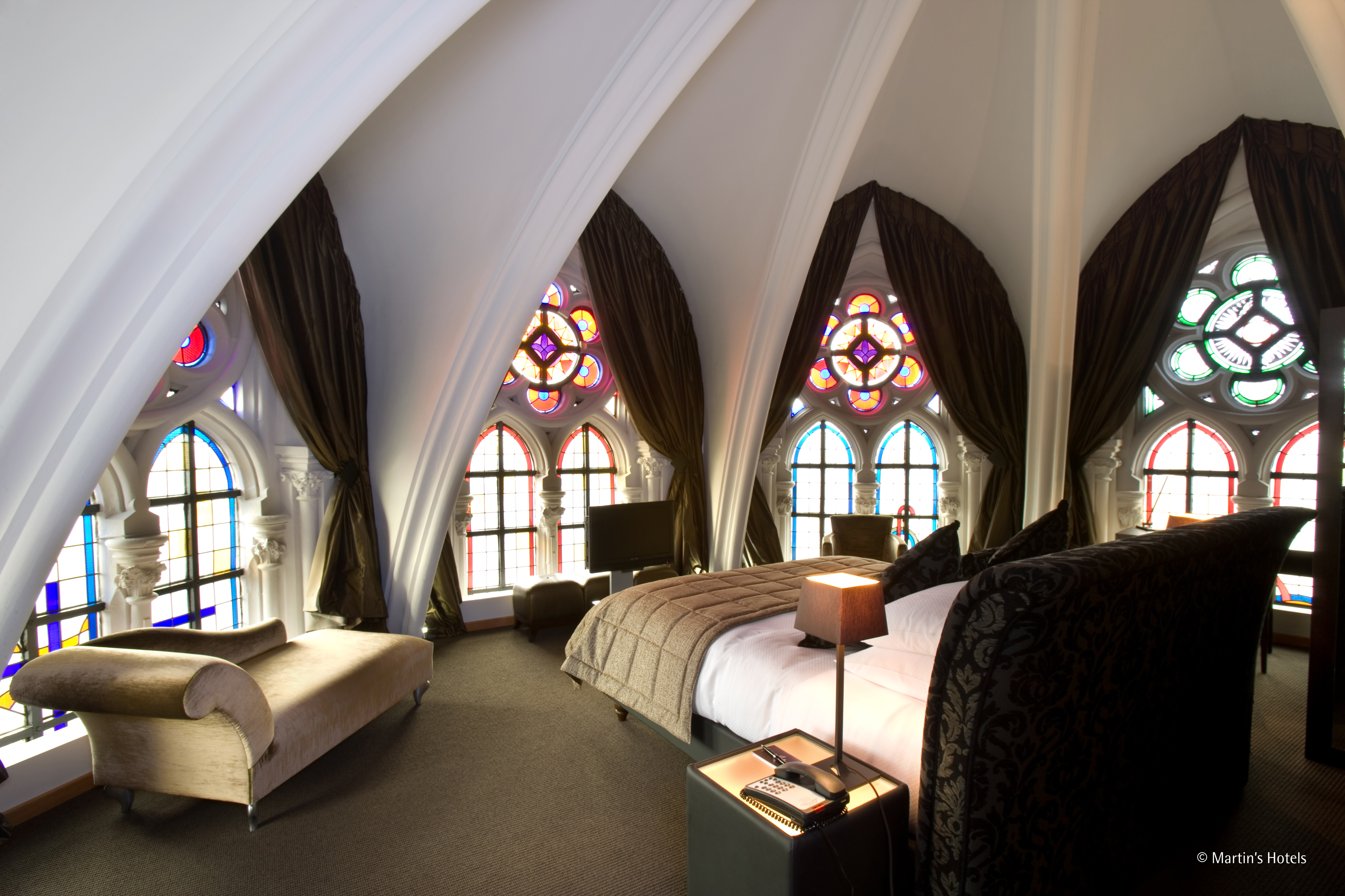 Ein luxuriöses Schlafzimmer in einer Kirche mit bunten Glasfenstern, hohen Decken und eleganten Möbeln.