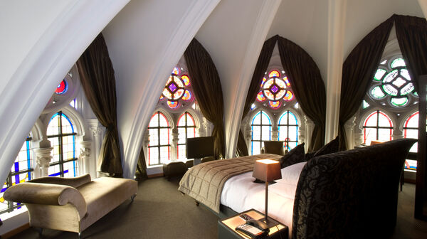 Ein luxuriöses Schlafzimmer in einer Kirche mit bunten Glasfenstern, hohen Decken und eleganten Möbeln.