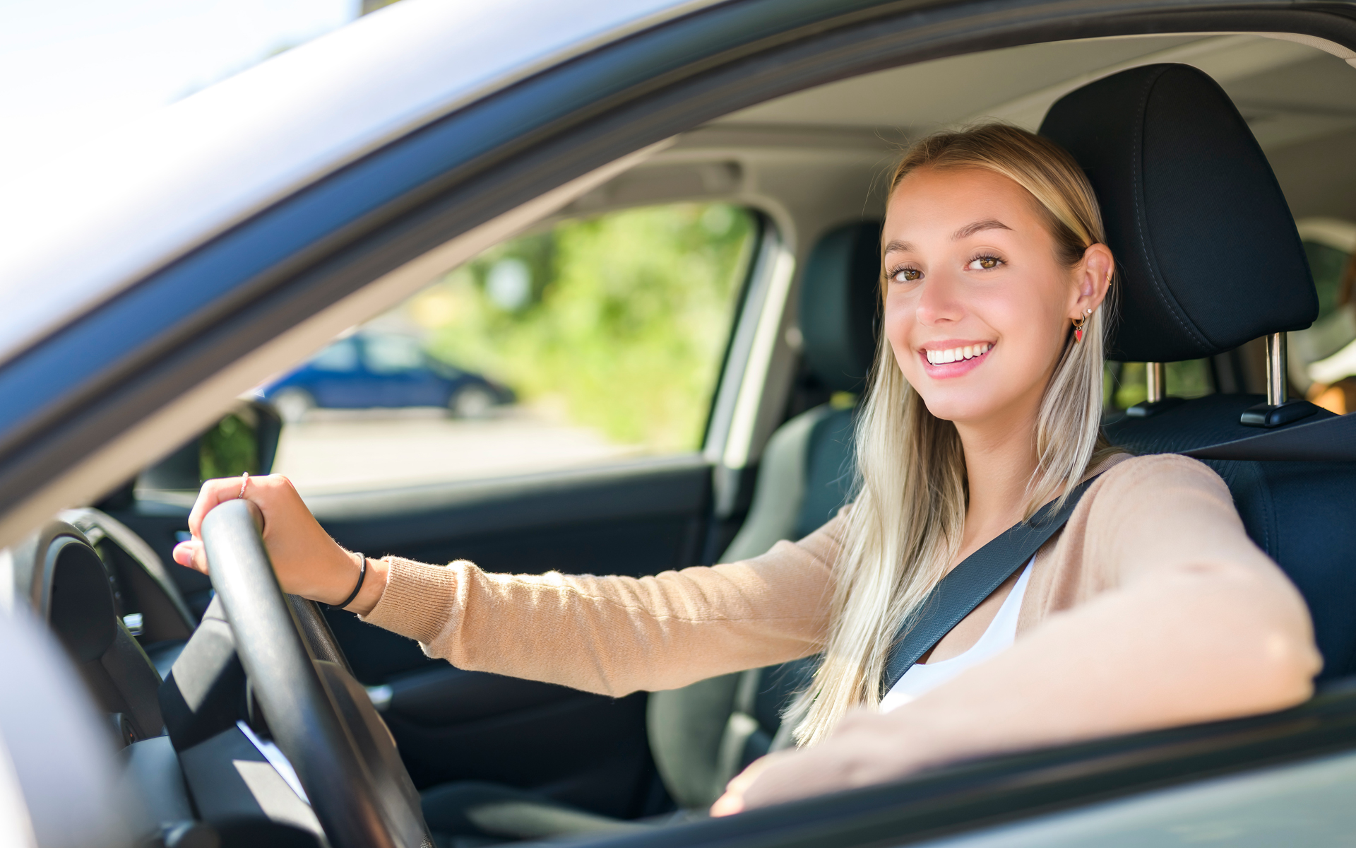 Junge Frau am Steuer im Auto, sie schaut nach links aus dem Fenster und lacht.