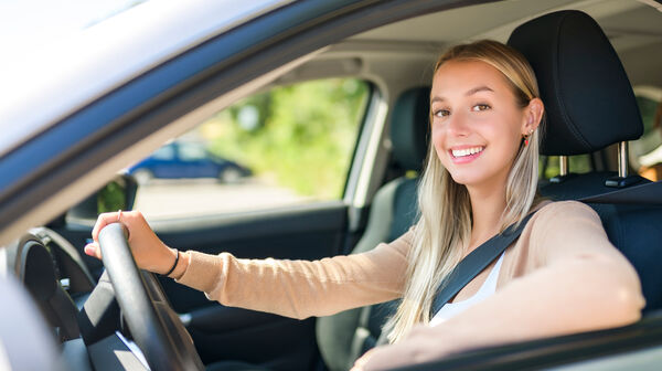 Junge Frau am Steuer im Auto, sie schaut nach links aus dem Fenster und lacht.