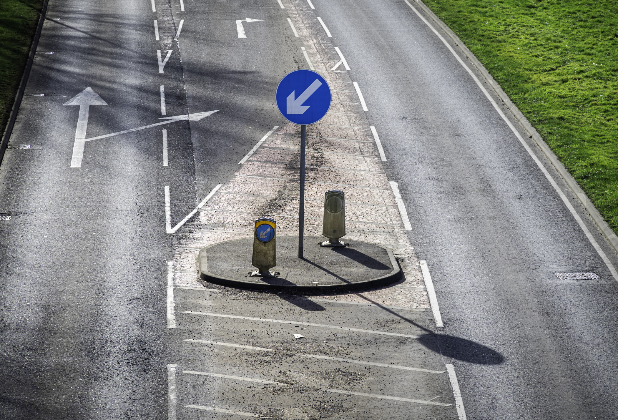 Eine Straße an der Linksverkehr herrscht. Eine Straßenschild auf dem ein Pfeil abgebildet ist, der nach links unten zeigt.