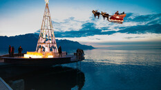 Ein beleuchteter Weihnachtsbaum auf einem Steg am Meer, mit einem fliegenden Weihnachtsmannschlitten im Hintergrund.
