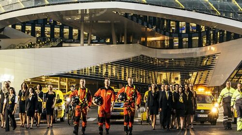 Die ÖAMTC Flotte vor dem Mobilitätszentrum. Viele Personen in Dienstkleidung: Kfz-Techniker:innen, Pilot:innen, Schalterdienstmitarbeiter:innen.