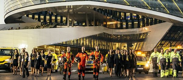 Die ÖAMTC Flotte vor dem Mobilitätszentrum. Viele Personen in Dienstkleidung: Kfz-Techniker:innen, Pilot:innen, Schalterdienstmitarbeiter:innen.