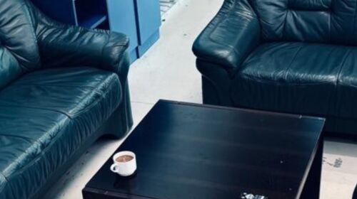 2 schwarze Sofas rund um einen schwarzen Beistelltisch, auf dem eine Tasse Kaffee steht.