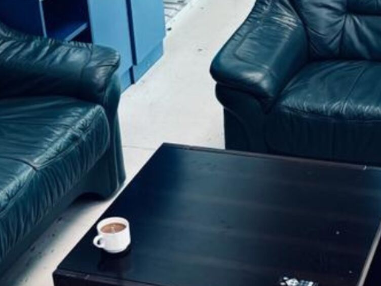 Hotel Stützpunkt 2 schwarze Sofas rund um einen schwarzen Beistelltisch, auf dem eine Tasse Kaffee steht.
