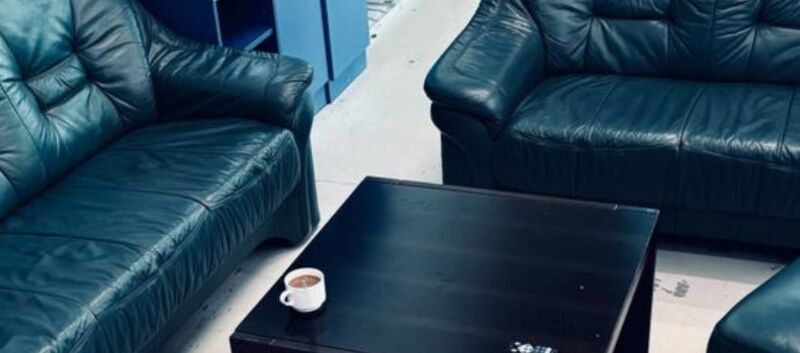 2 schwarze Sofas rund um einen schwarzen Beistelltisch, auf dem eine Tasse Kaffee steht.