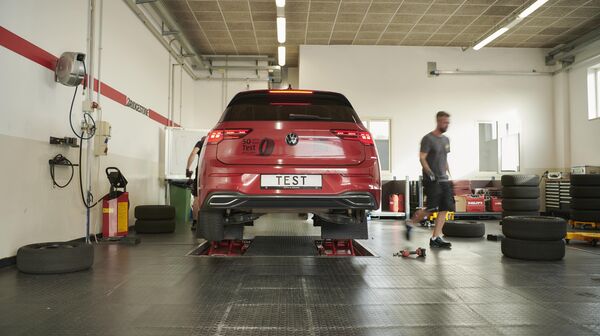 Sommerreifentest - Auto in Werkstatt ist auf der Hebebühne, rechts im Bild sieht man einzelne Reifen, Werkzeug und einen Mann.