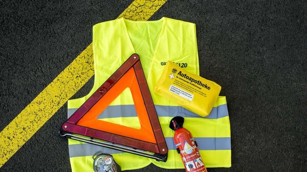 Pflichtausstattung für Autofahrer auf dem Boden eines Parkplatzes ausgelegt: Warnweste, Warndreieck, Verbandszeug und Ersatzlampenset