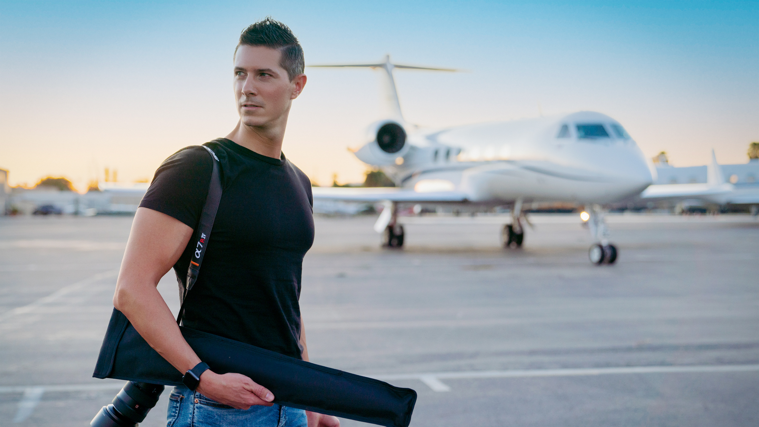 Fotograf Daniel Gossmann steht mit Kamera auf einem Flughafen, im Hintergrund ein Jet.