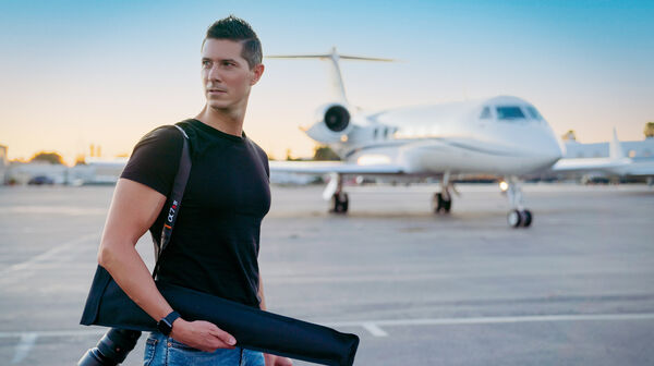 Fotograf Daniel Gossmann steht mit Kamera auf einem Flughafen, im Hintergrund ein Jet.