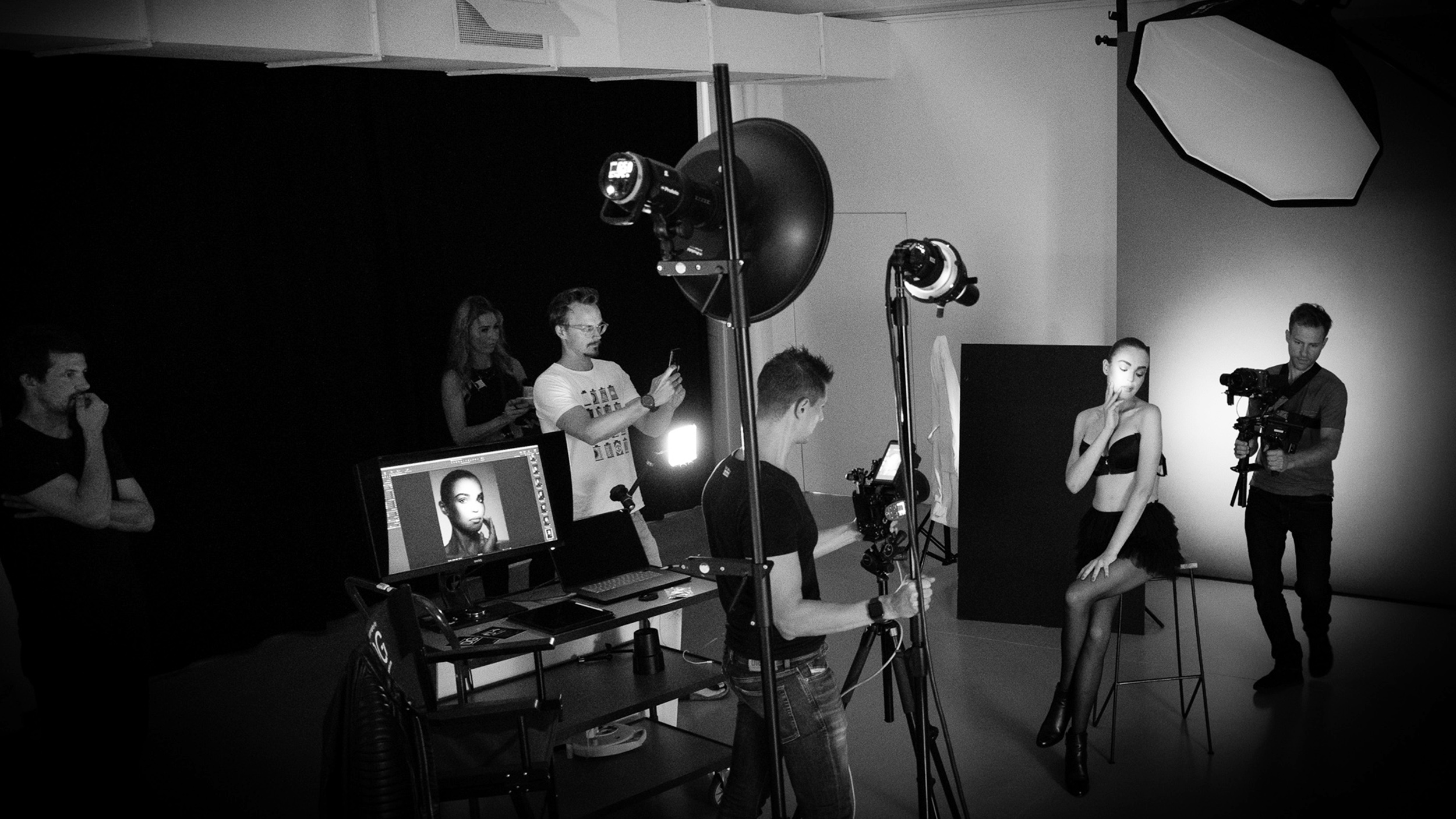 Schwarzweiß-Foto von einem Studio-Fotoshooting. Im Vordergrund der Fotograf, das Model wird ausgeleuchtet.