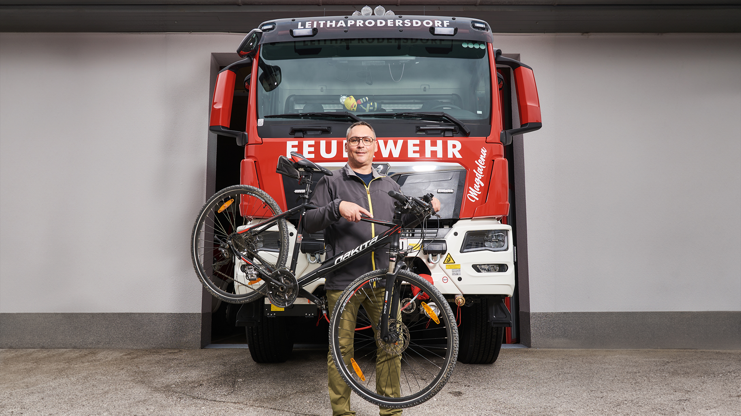 Feuerwehrmann Hannes Heiss steht vor einem Feuerwehrauto. Neben ihm sein Fahrrad.