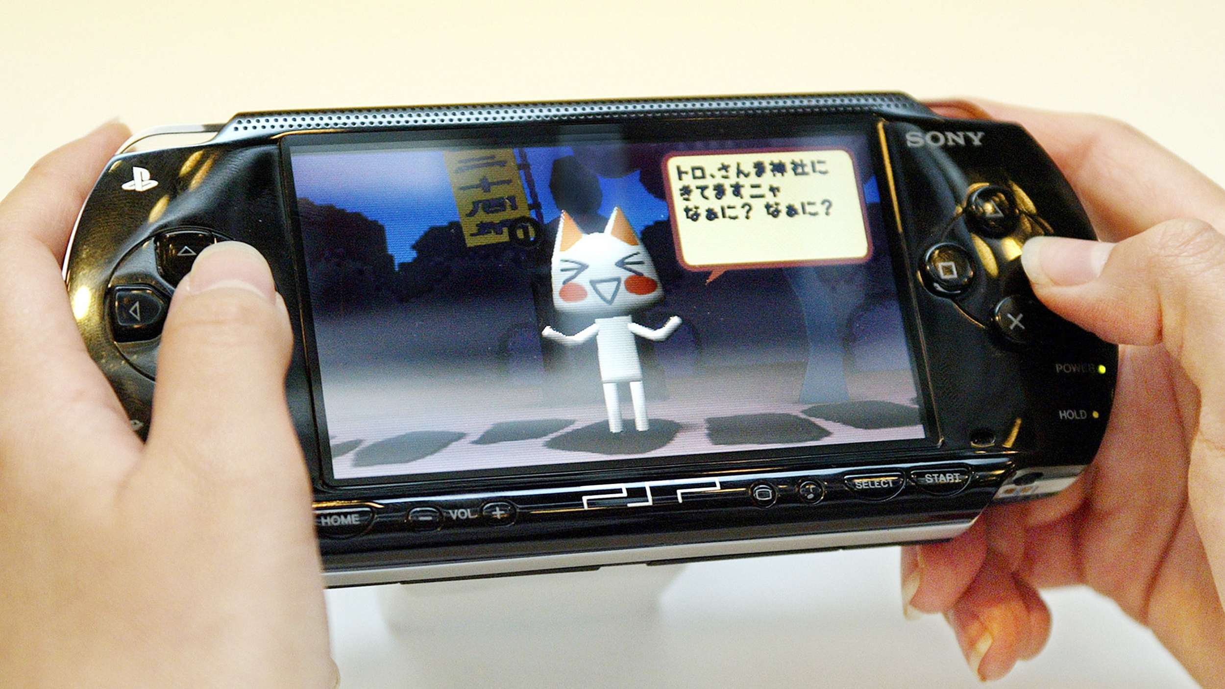 Schwarze Handheldkonsole, die PSP von Sony, wird von jemandem gehalten, von der Person sind aber nur die Hände zu sehen.Am Bildschirm sieht man eine animierte Katze.