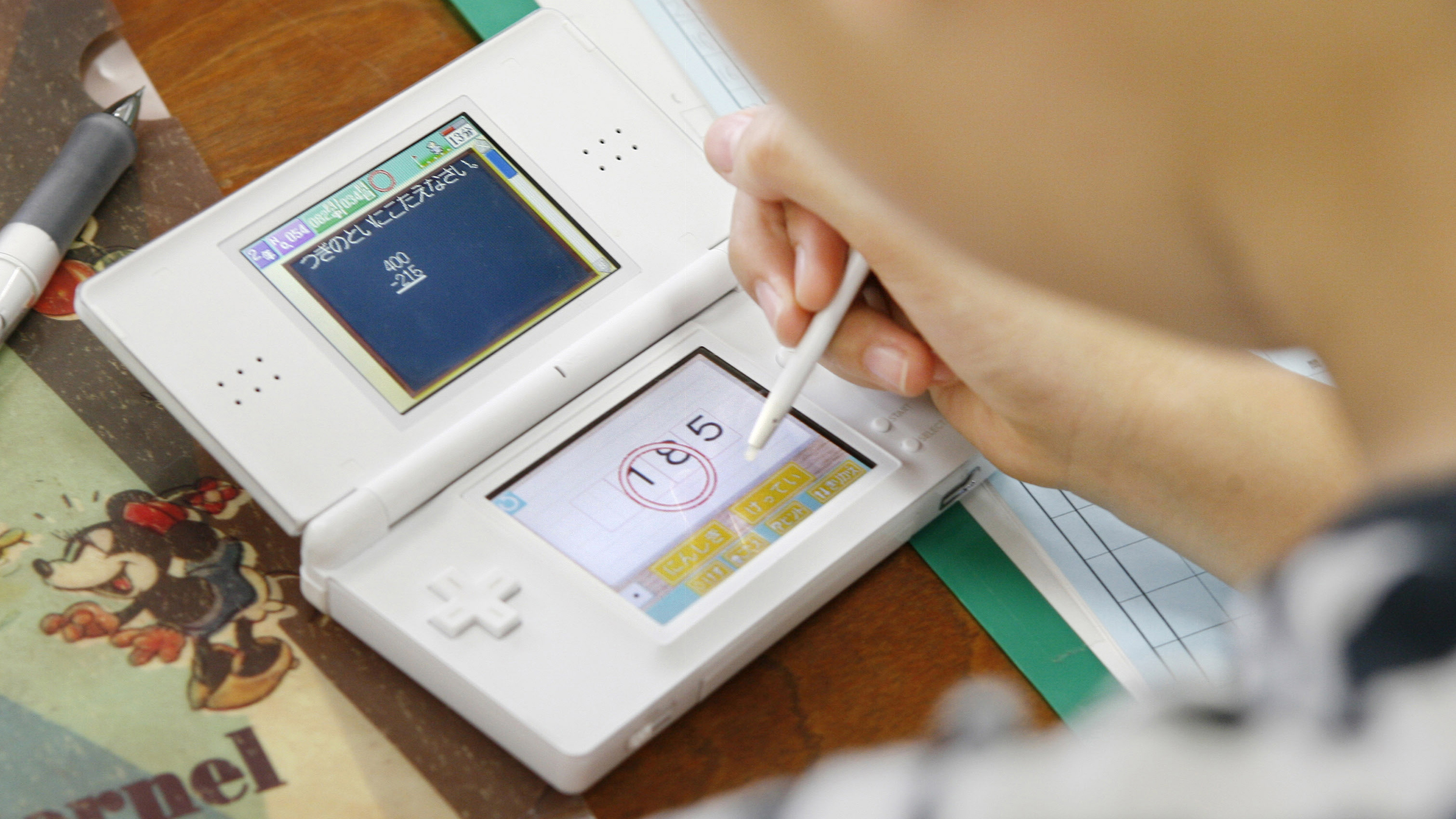 Ein Mädchen spielt mit einem weißen Nintendo DS und übt damit Mathe.