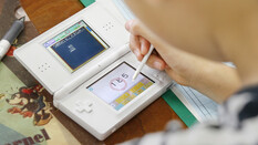 Ein Mädchen spielt mit einem weißen Nintendo DS und übt damit Mathe.