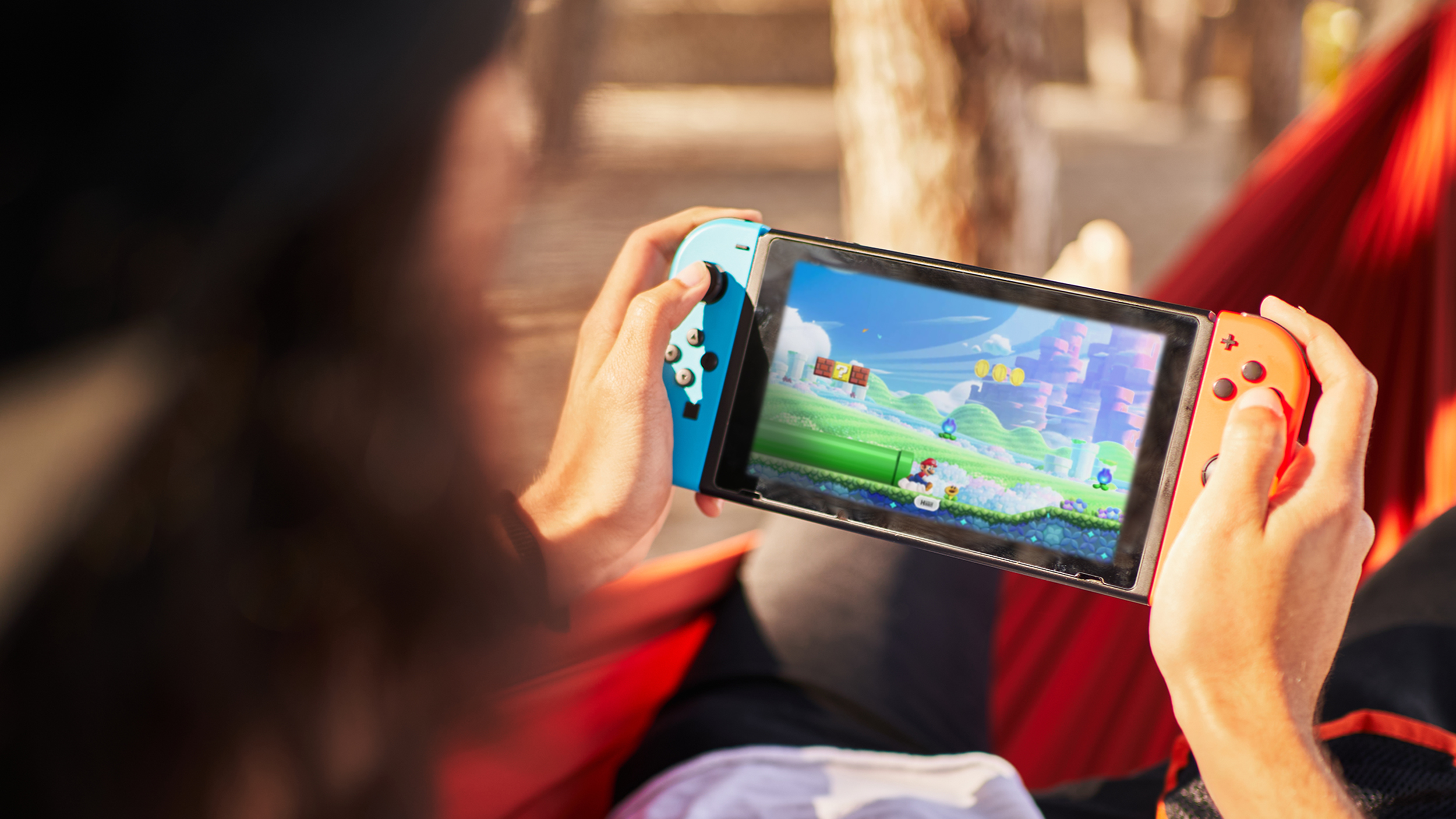 Nicht erkennbare Person mit einer Verschlusskappe, die Videospiele auf einer tragbaren Konsole spielt, während sie auf Hängematte hängt.