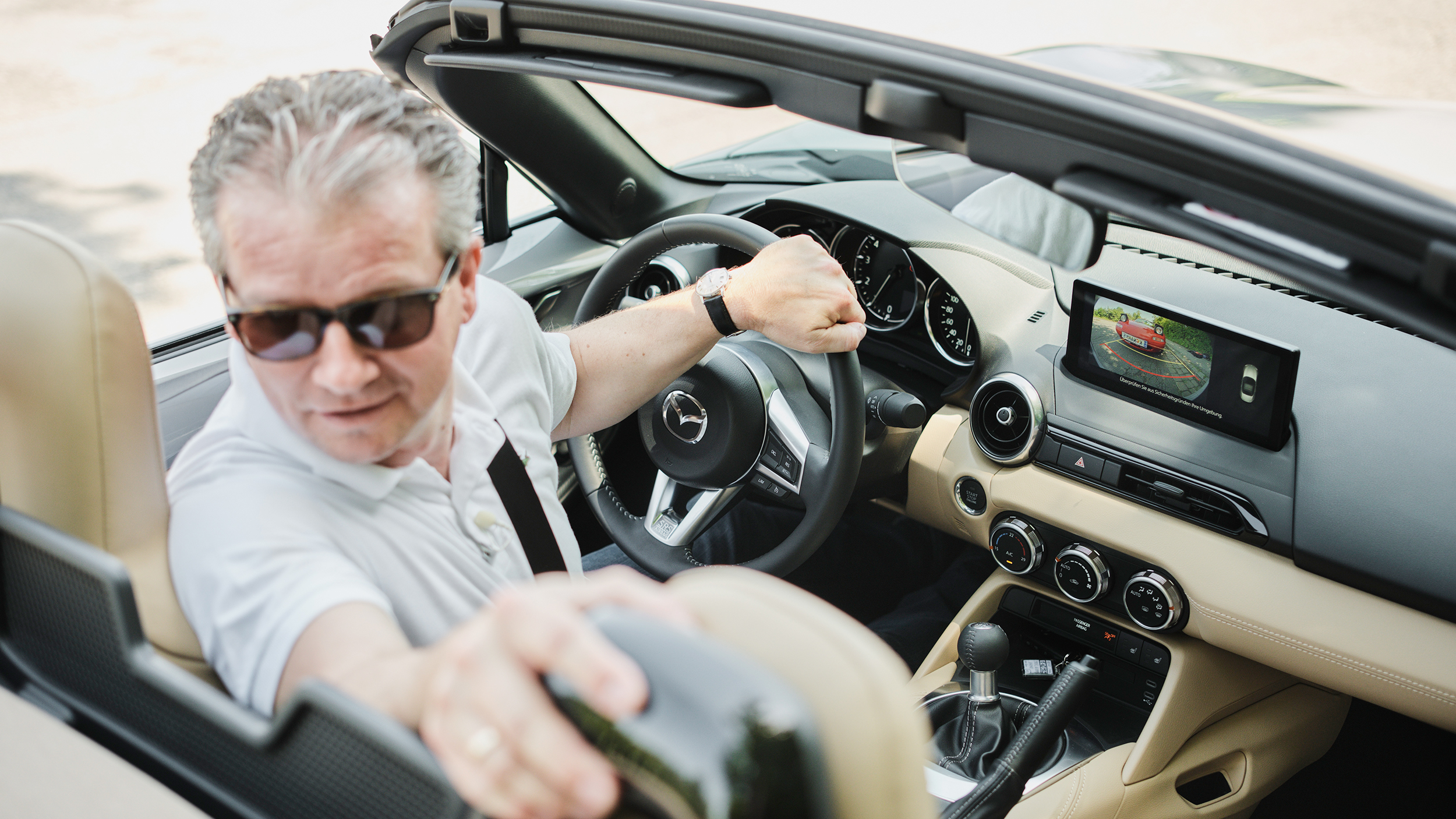 Eine Person fährt in einem Cabrio retour und blickt deshalb zurück.